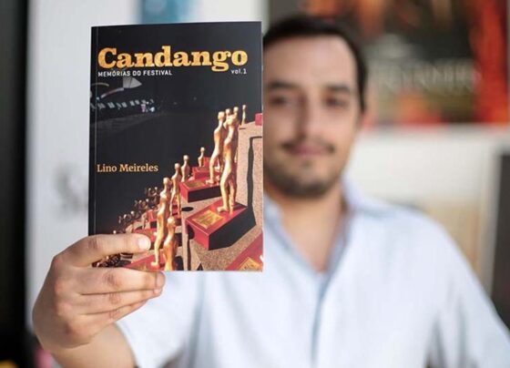 Foto colorida de Lino Meireles segurando livro - Metrópoles